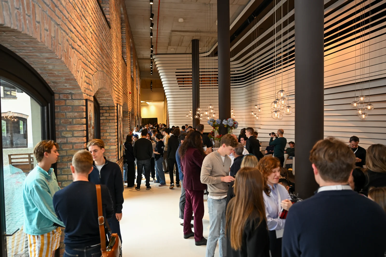 Guests and students mingling in a brick-walled venue hallway at a BBICC event